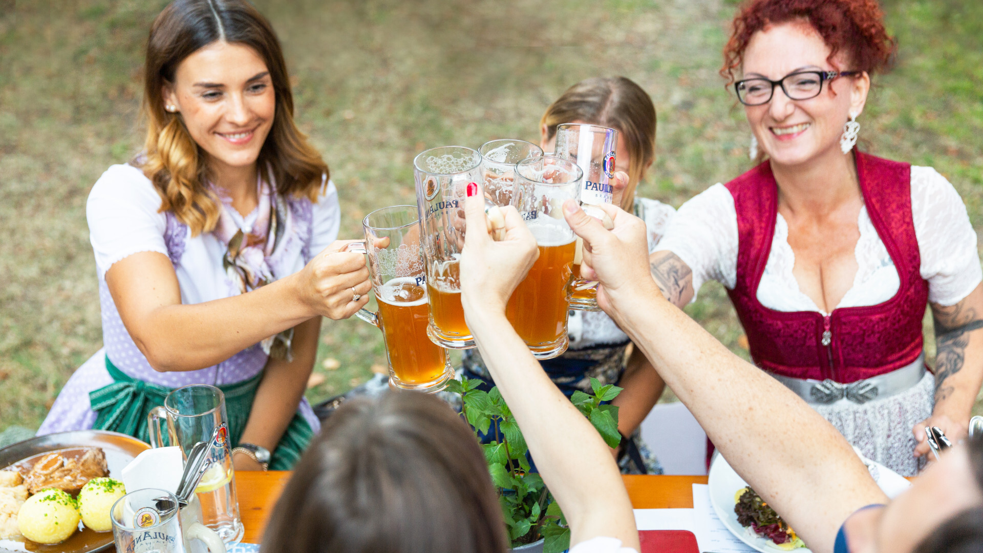 Biergarten-Kultur: Frauen, die im Dirndl mit Bier im Biergarten anstoßen